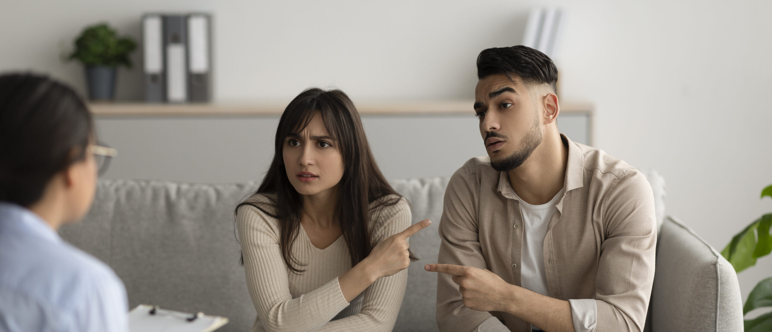 Unhappy arab spouses blaming each other in relationship problems on meeting with marital counselor, having conflict at phychologist's office